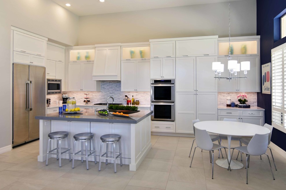 Inspiration for a large classic u-shaped kitchen/diner in Phoenix with a submerged sink, recessed-panel cabinets, white cabinets, engineered stone countertops, white splashback, stone tiled splashback, stainless steel appliances, porcelain flooring, an island, beige floors and grey worktops.