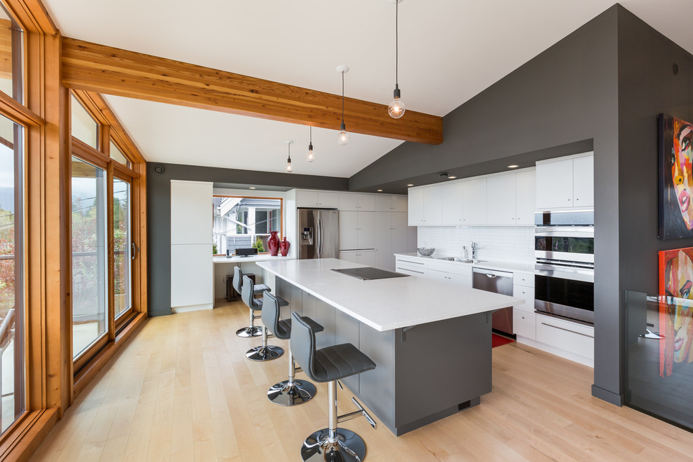 This is an example of a contemporary grey and white l-shaped open plan kitchen in Vancouver with flat-panel cabinets, white cabinets, white splashback, light hardwood flooring and an island.