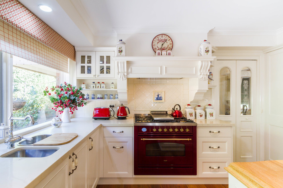 Bild på ett avskilt, stort lantligt beige beige u-kök, med en undermonterad diskho, skåp i shakerstil, vita skåp, träbänkskiva, vitt stänkskydd, stänkskydd i keramik, färgglada vitvaror, mellanmörkt trägolv, en köksö och brunt golv