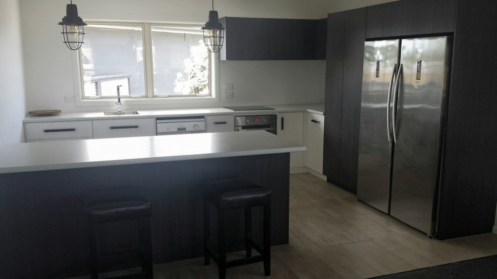 Large contemporary l-shaped open plan kitchen in Christchurch with a single-bowl sink, flat-panel cabinets, dark wood cabinets, laminate countertops, white splashback, glass sheet splashback, stainless steel appliances, ceramic flooring, a breakfast bar and grey floors.