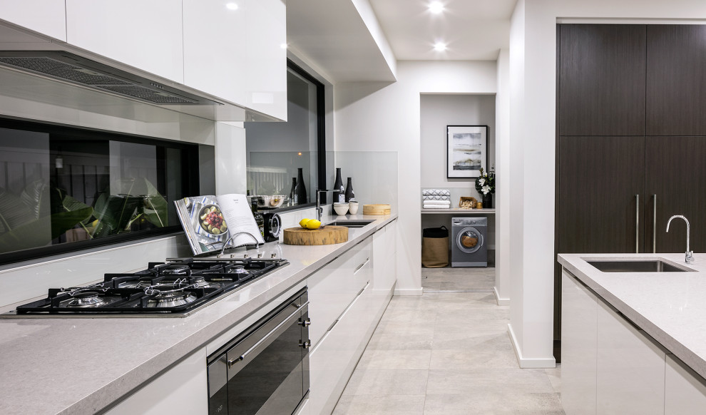 Modern inredning av ett stort grå grått l-kök, med en dubbel diskho, släta luckor, vita skåp, fönster som stänkskydd, en köksö och grått golv