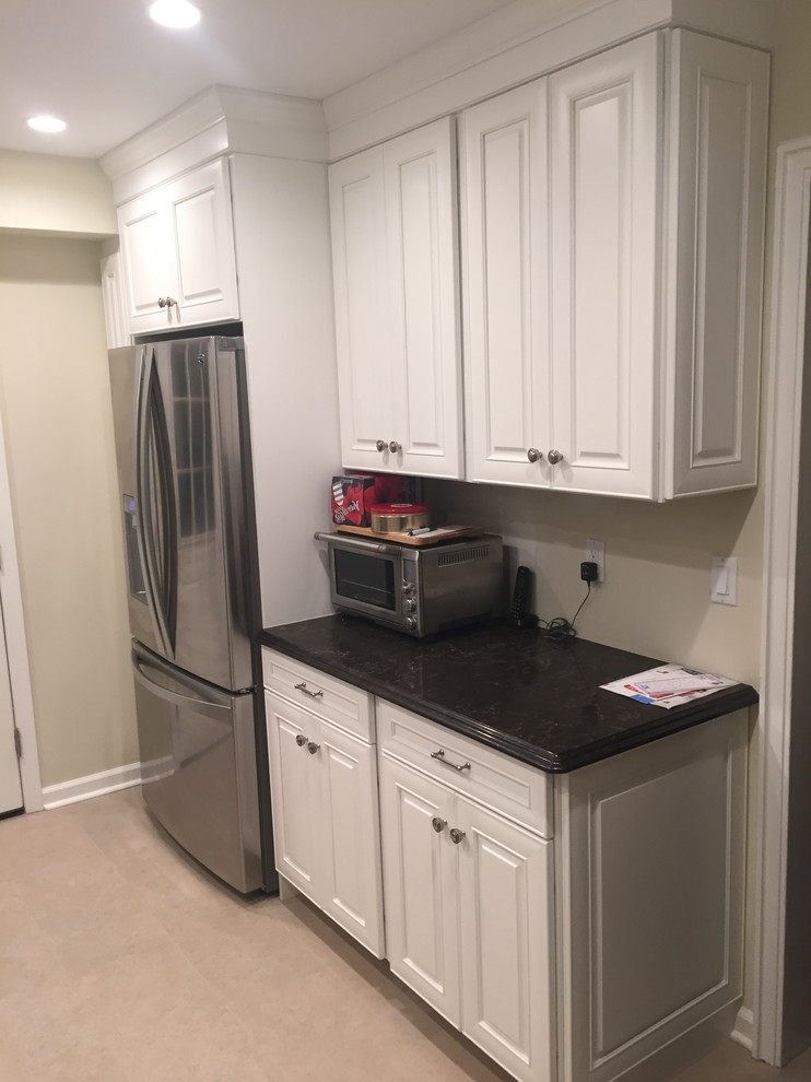 Photo of a traditional kitchen in New York with raised-panel cabinets, white cabinets, stainless steel appliances and beige floors.