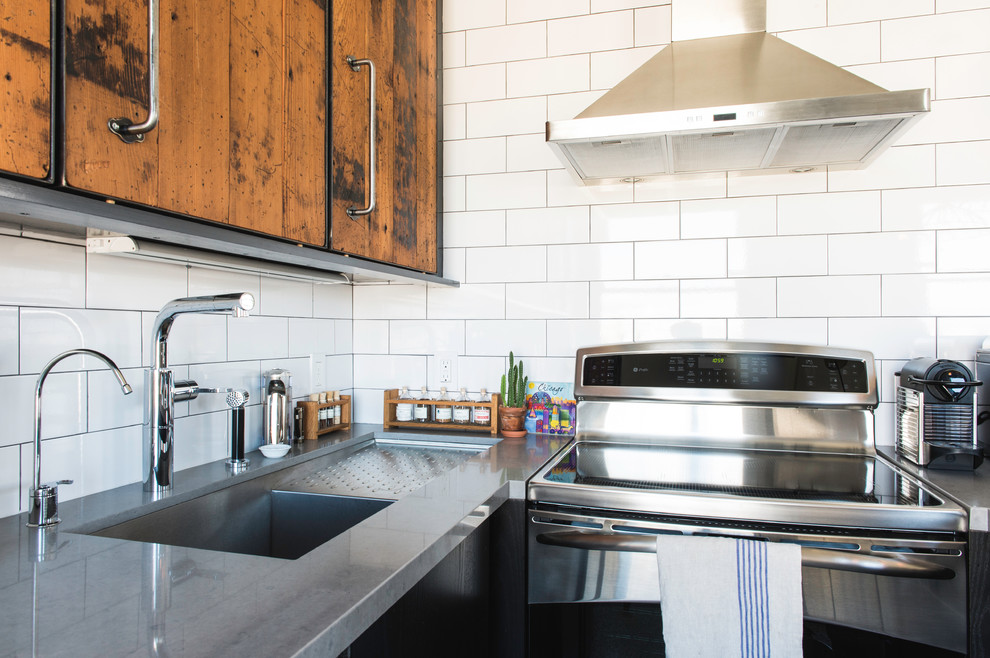 Enclosed kitchen - mid-sized industrial u-shaped enclosed kitchen idea in San Francisco with an undermount sink, flat-panel cabinets, black cabinets, quartz countertops, white backsplash, subway tile backsplash, stainless steel appliances and a peninsula