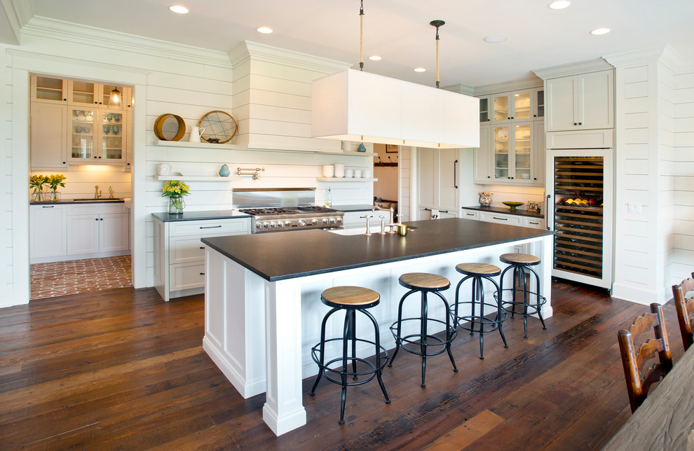 Farmhouse l-shaped medium tone wood floor eat-in kitchen photo in Nashville with a farmhouse sink, shaker cabinets, white cabinets, soapstone countertops, white backsplash, stainless steel appliances and an island