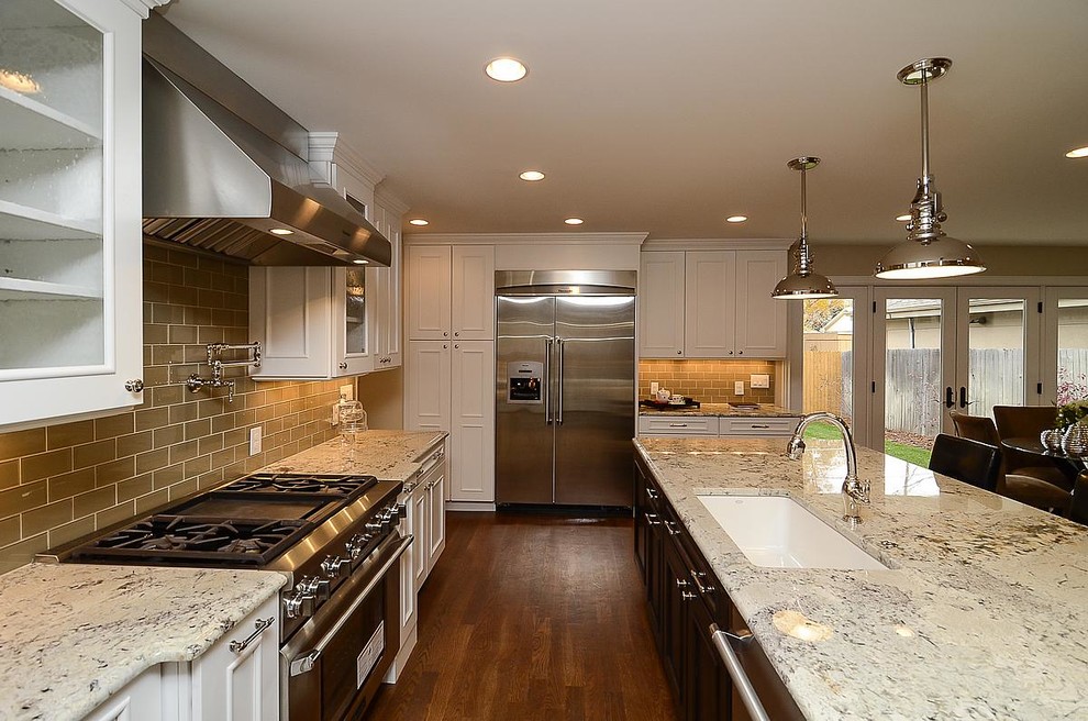 Large elegant l-shaped medium tone wood floor and brown floor enclosed kitchen photo in Orlando with an undermount sink, glass-front cabinets, white cabinets, granite countertops, beige backsplash, subway tile backsplash, stainless steel appliances and an island