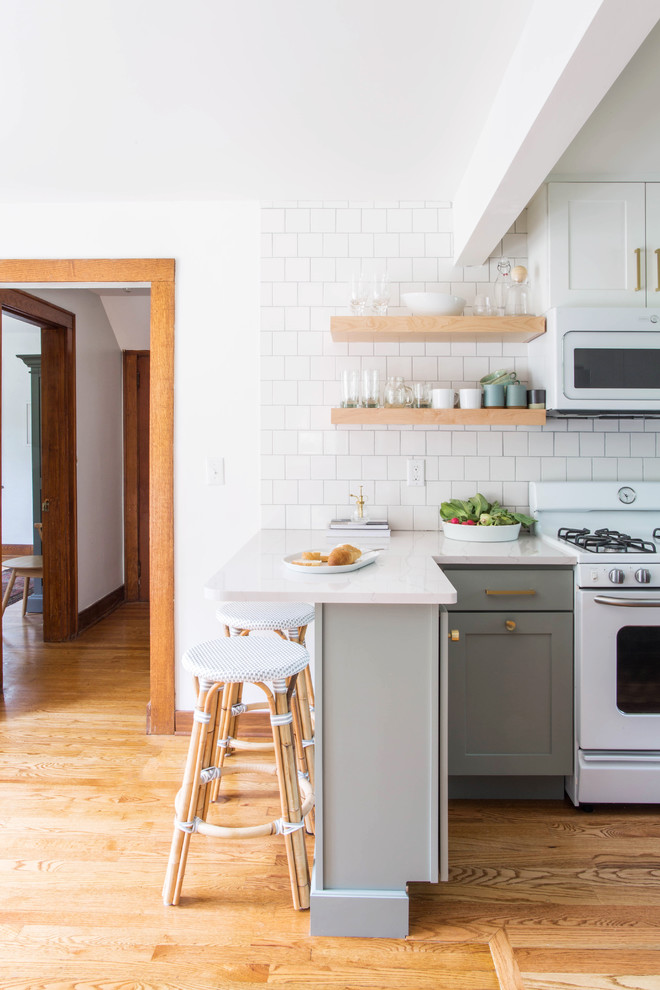 Small transitional u-shaped medium tone wood floor and brown floor eat-in kitchen photo in Other with a farmhouse sink, shaker cabinets, blue cabinets, quartz countertops, white backsplash, porcelain backsplash, white appliances and a peninsula