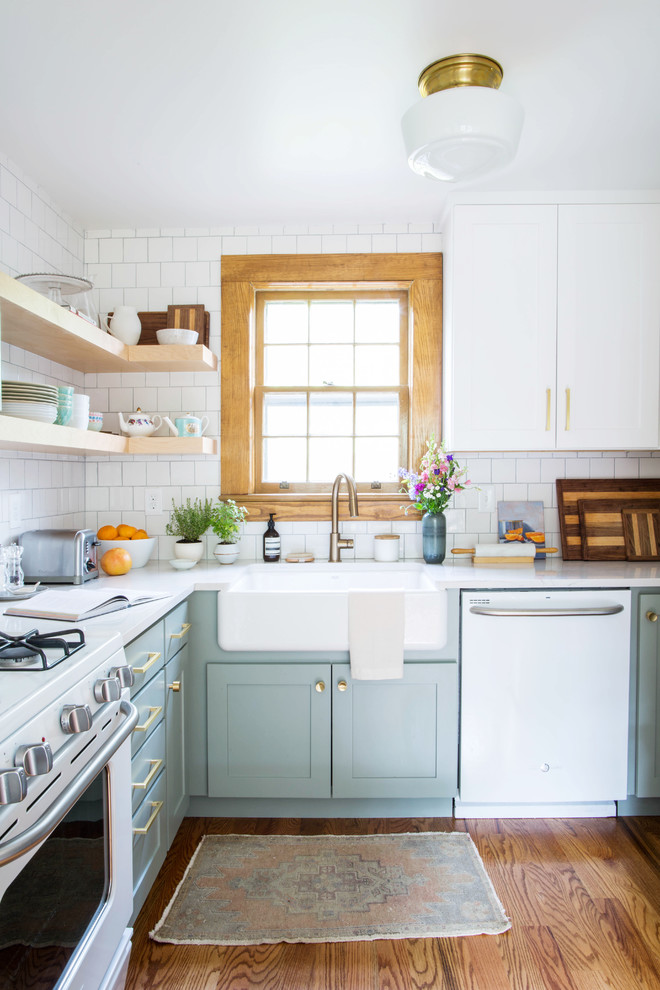 Example of a small transitional u-shaped medium tone wood floor and brown floor eat-in kitchen design in Other with a farmhouse sink, shaker cabinets, blue cabinets, quartz countertops, white backsplash, porcelain backsplash, white appliances and a peninsula