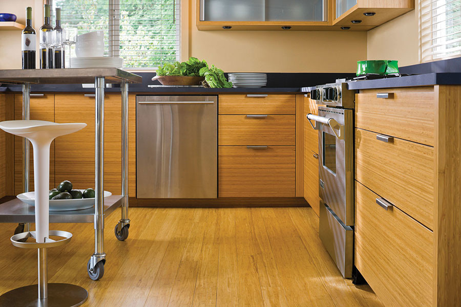 Photo of a small world-inspired u-shaped kitchen/diner in Chicago with flat-panel cabinets, light wood cabinets, soapstone worktops, black splashback, stainless steel appliances, bamboo flooring and an island.