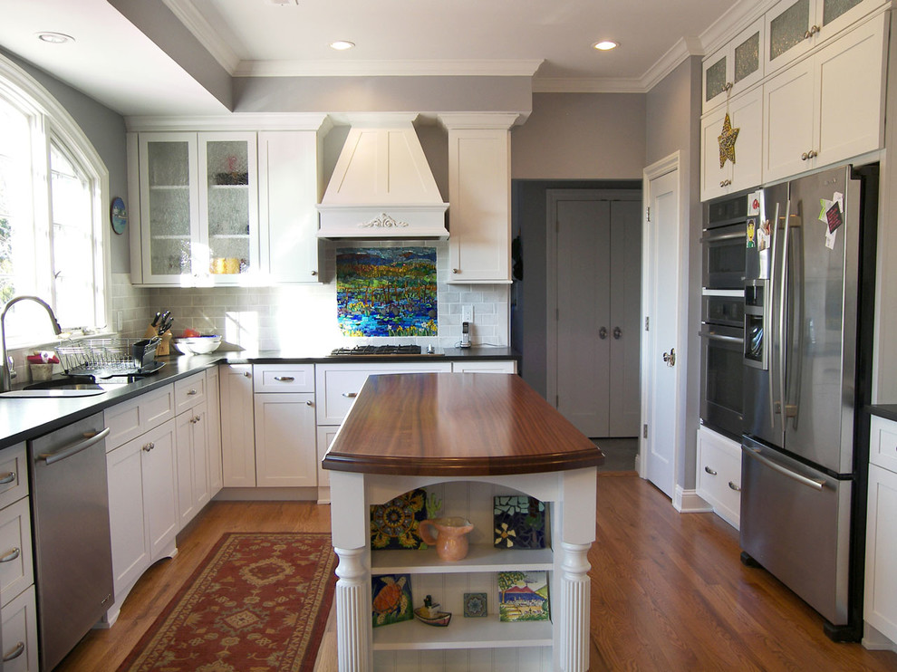 Immagine di una cucina a L design con ante bianche, paraspruzzi bianco, paraspruzzi con piastrelle di cemento, elettrodomestici in acciaio inossidabile e pavimento in legno massello medio