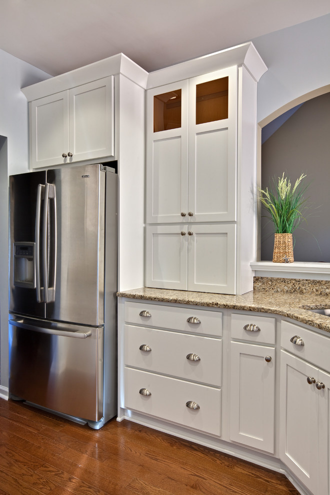 Inredning av ett modernt litet beige beige kök, med skåp i shakerstil, vita skåp, rostfria vitvaror, en dubbel diskho, granitbänkskiva, mellanmörkt trägolv, en halv köksö och brunt golv