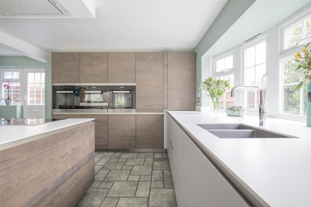 This is an example of a medium sized contemporary u-shaped kitchen in Sussex with an integrated sink, flat-panel cabinets, medium wood cabinets, composite countertops, integrated appliances and an island.