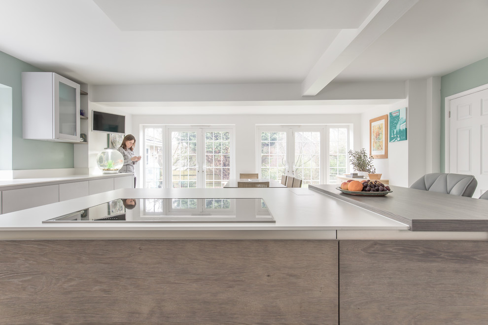 This is an example of a medium sized contemporary u-shaped kitchen in Sussex with an integrated sink, flat-panel cabinets, medium wood cabinets, composite countertops, integrated appliances and an island.