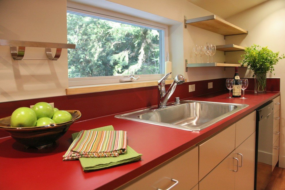 Стильный дизайн: параллельная кухня-гостиная в современном стиле с одинарной мойкой, бежевыми фасадами, столешницей из ламината, красным фартуком, черной техникой и плоскими фасадами - последний тренд