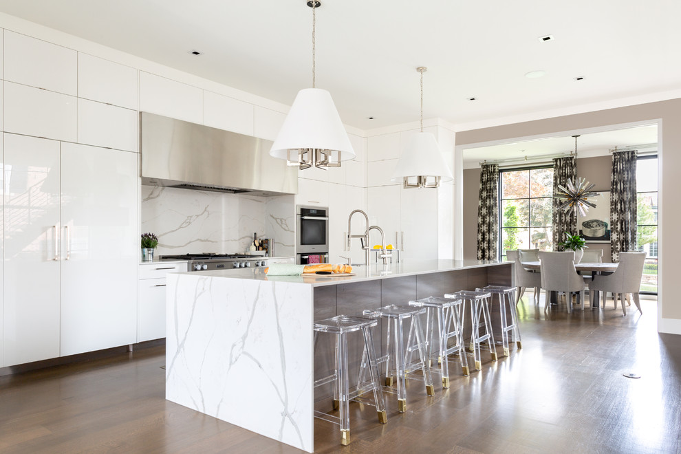 Modern inredning av ett avskilt, stort vit vitt u-kök, med en undermonterad diskho, släta luckor, vita skåp, bänkskiva i kvartsit, vitt stänkskydd, stänkskydd i sten, rostfria vitvaror, ljust trägolv, en köksö och brunt golv