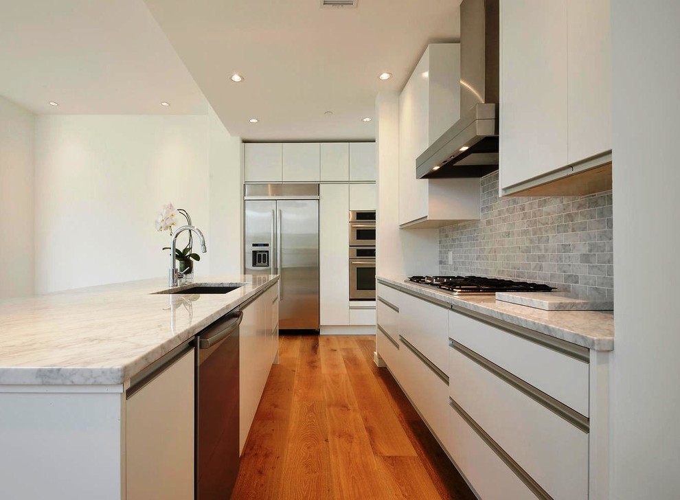 Photo of a medium sized modern galley open plan kitchen in Austin with a submerged sink, flat-panel cabinets, white cabinets, marble worktops, grey splashback, stone tiled splashback, stainless steel appliances, dark hardwood flooring, an island and brown floors.