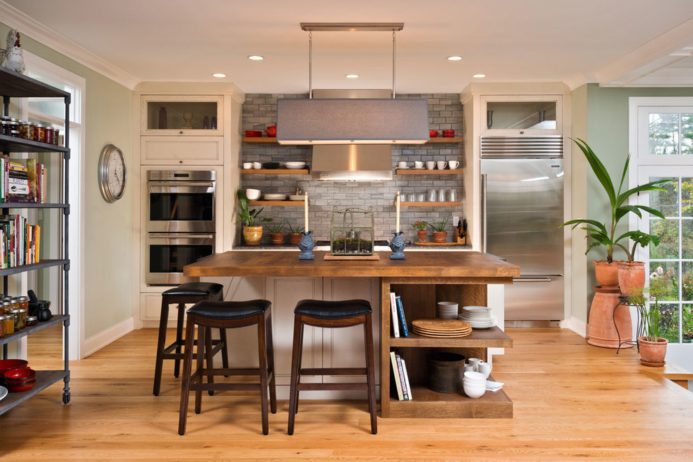 Exempel på ett lantligt kök, med luckor med infälld panel, vita skåp, grått stänkskydd, rostfria vitvaror, mellanmörkt trägolv och en köksö
