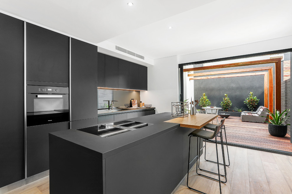 Inspiration for a contemporary kitchen in Sydney with a single-bowl sink, flat-panel cabinets, black cabinets, mirror splashback, black appliances, an island, black worktops, medium hardwood flooring and brown floors.