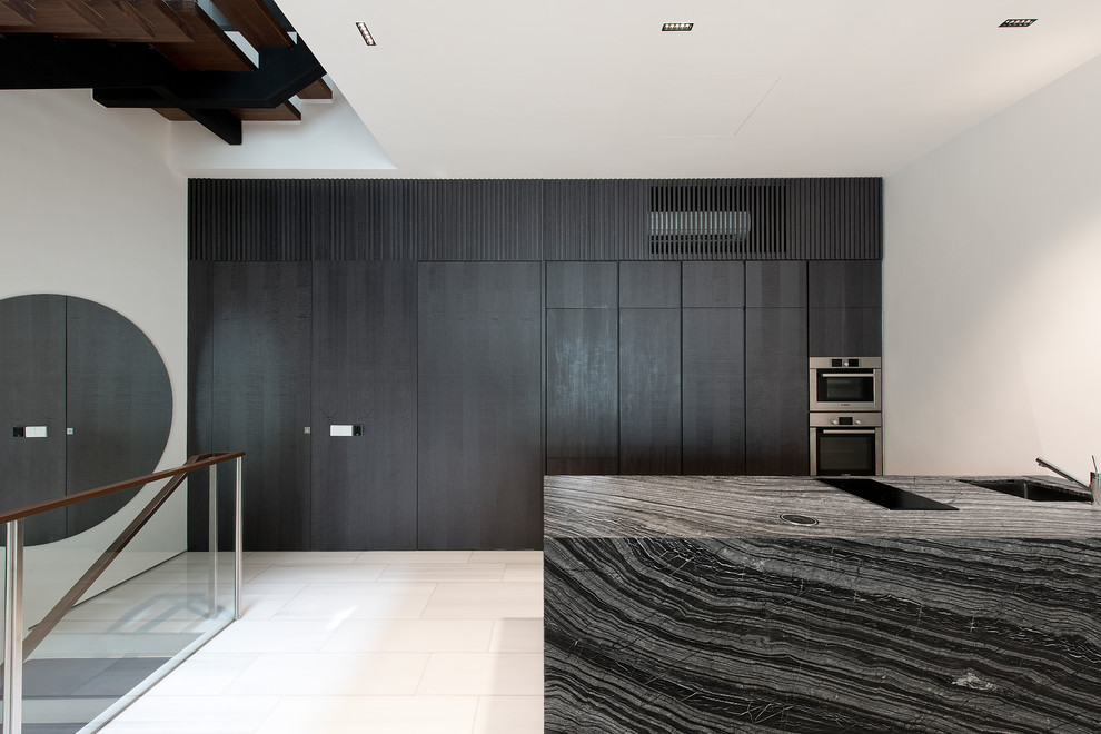 This is an example of a contemporary galley kitchen in Singapore with a single-bowl sink, flat-panel cabinets, dark wood cabinets, integrated appliances, a breakfast bar, white floors and black worktops.