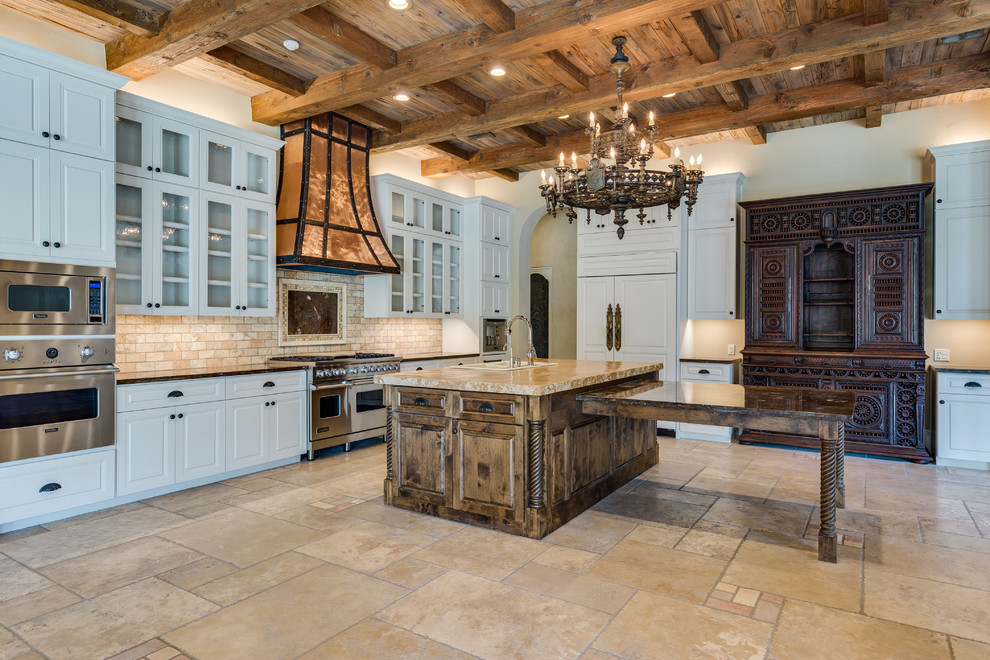 Huge tuscan u-shaped travertine floor and beige floor enclosed kitchen photo in Austin with a drop-in sink, raised-panel cabinets, white cabinets, granite countertops, beige backsplash, stone tile backsplash, stainless steel appliances and two islands
