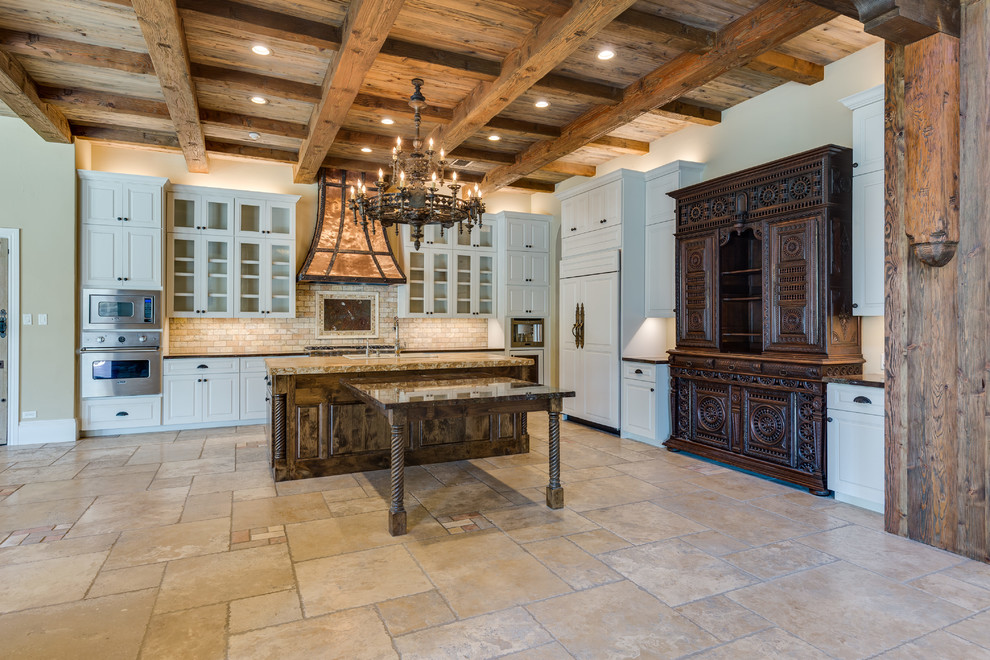 Inspiration for a huge mediterranean travertine floor and beige floor enclosed kitchen remodel in Austin with a drop-in sink, raised-panel cabinets, white cabinets, granite countertops, beige backsplash, stone tile backsplash, paneled appliances and two islands