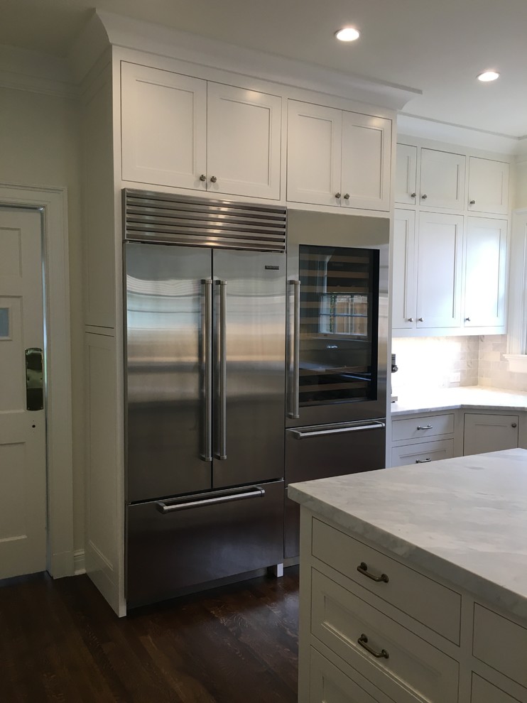 Large classic u-shaped enclosed kitchen in Austin with a submerged sink, recessed-panel cabinets, white cabinets, marble worktops, white splashback, marble splashback, stainless steel appliances, dark hardwood flooring, an island, brown floors and white worktops.