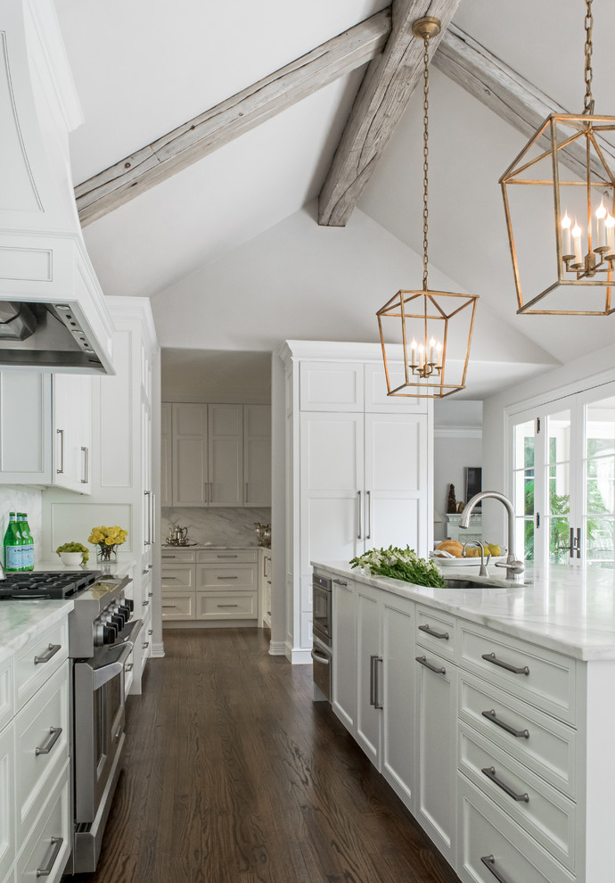 Design ideas for a classic galley open plan kitchen in Austin with a single-bowl sink, recessed-panel cabinets, white cabinets, marble worktops, white splashback, stone slab splashback, integrated appliances, medium hardwood flooring and an island.