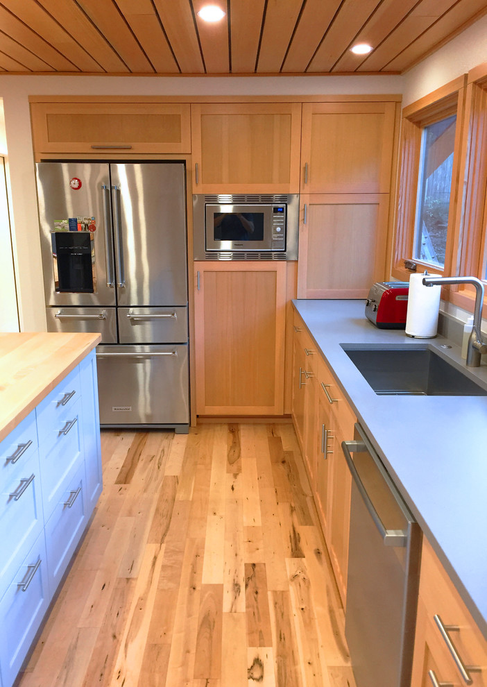 Idéer för att renovera ett mellanstort funkis kök, med en undermonterad diskho, släta luckor, skåp i ljust trä, bänkskiva i kvarts, grått stänkskydd, rostfria vitvaror, ljust trägolv och en köksö