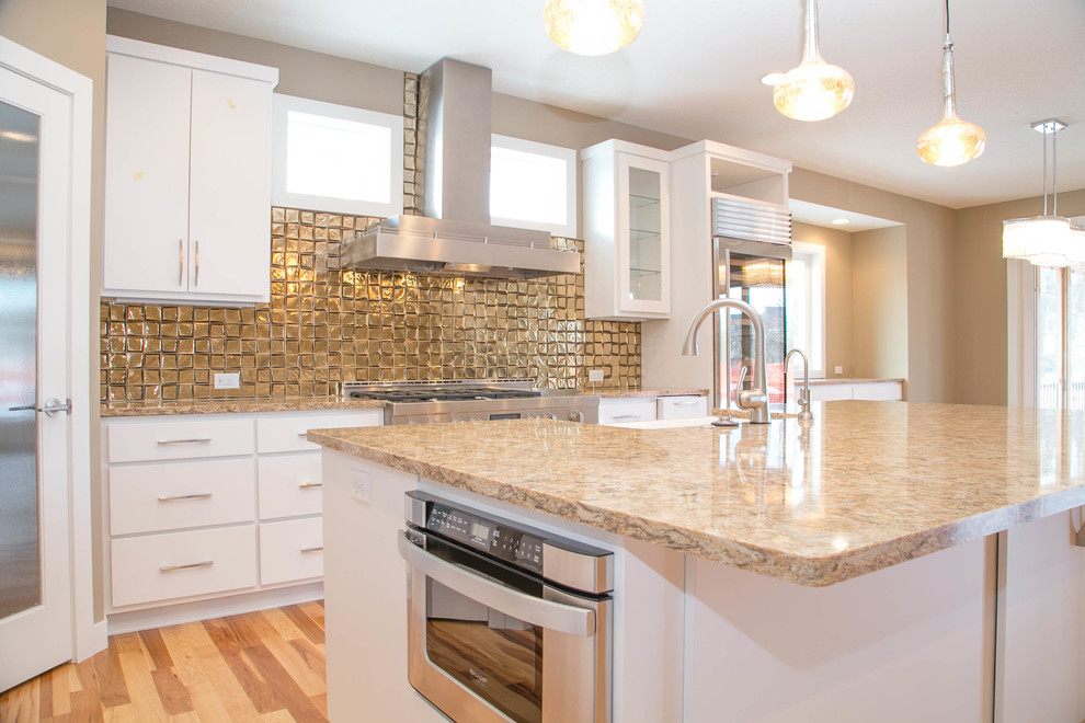 Traditional l-shaped kitchen/diner in Minneapolis with a submerged sink, flat-panel cabinets, white cabinets, engineered stone countertops, metallic splashback, glass tiled splashback, stainless steel appliances, medium hardwood flooring and an island.