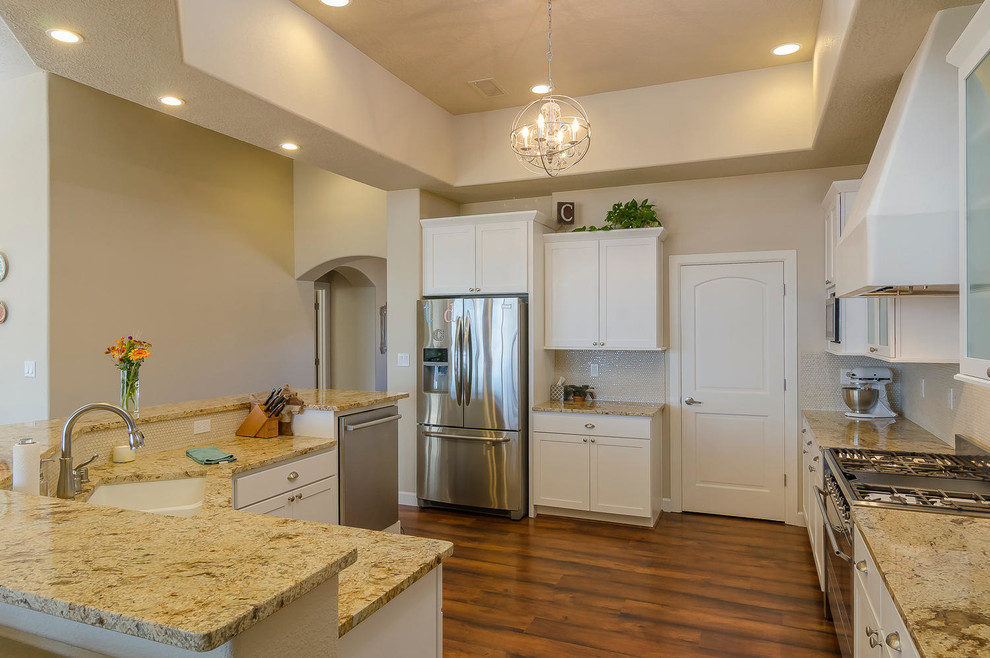 Kitchen pantry - mid-sized southwestern l-shaped kitchen pantry idea in Albuquerque with an undermount sink, shaker cabinets, white cabinets, granite countertops, beige backsplash, glass sheet backsplash, stainless steel appliances and an island