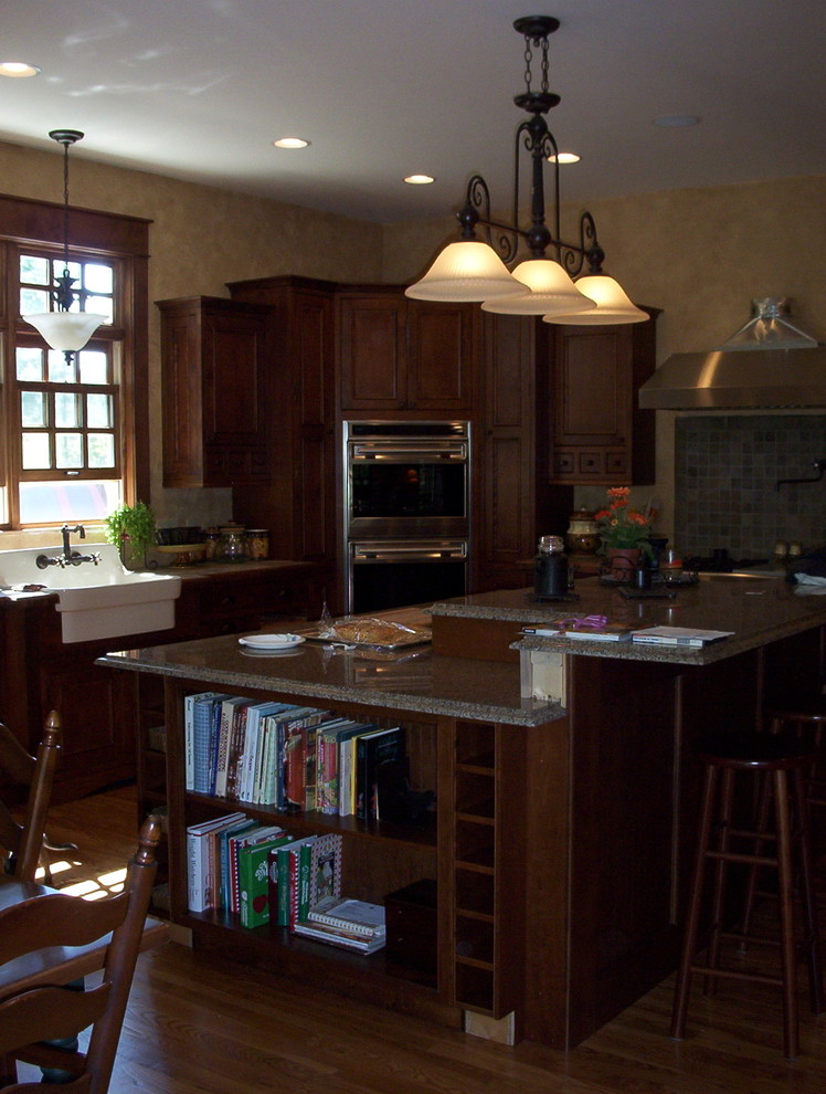 Klassisk inredning av ett stort kök, med en rustik diskho, luckor med infälld panel, skåp i mörkt trä, granitbänkskiva, flerfärgad stänkskydd, stänkskydd i keramik, integrerade vitvaror, mellanmörkt trägolv och en köksö