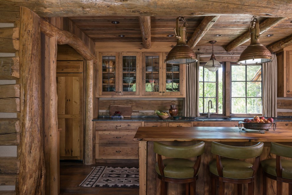 This is an example of a rustic kitchen in Other with glass-front cabinets, soapstone worktops, wood splashback, an island, a submerged sink, medium wood cabinets, dark hardwood flooring, brown floors and black worktops.