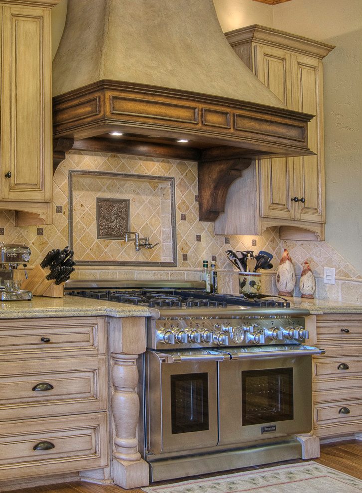 Enclosed kitchen - mid-sized mediterranean l-shaped medium tone wood floor enclosed kitchen idea in Austin with raised-panel cabinets, light wood cabinets, granite countertops, beige backsplash, stone tile backsplash, stainless steel appliances, an island and a double-bowl sink
