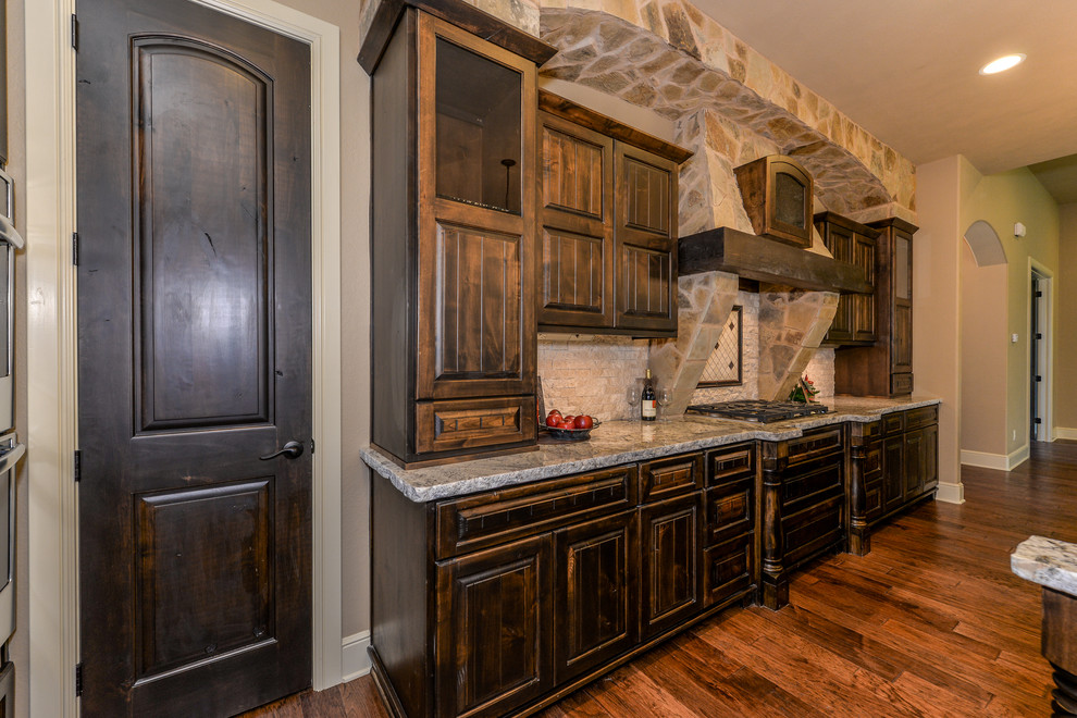 Photo of a large rustic open plan kitchen in Austin with a submerged sink, raised-panel cabinets, dark wood cabinets, granite worktops, white splashback, stone tiled splashback, stainless steel appliances, dark hardwood flooring and an island.