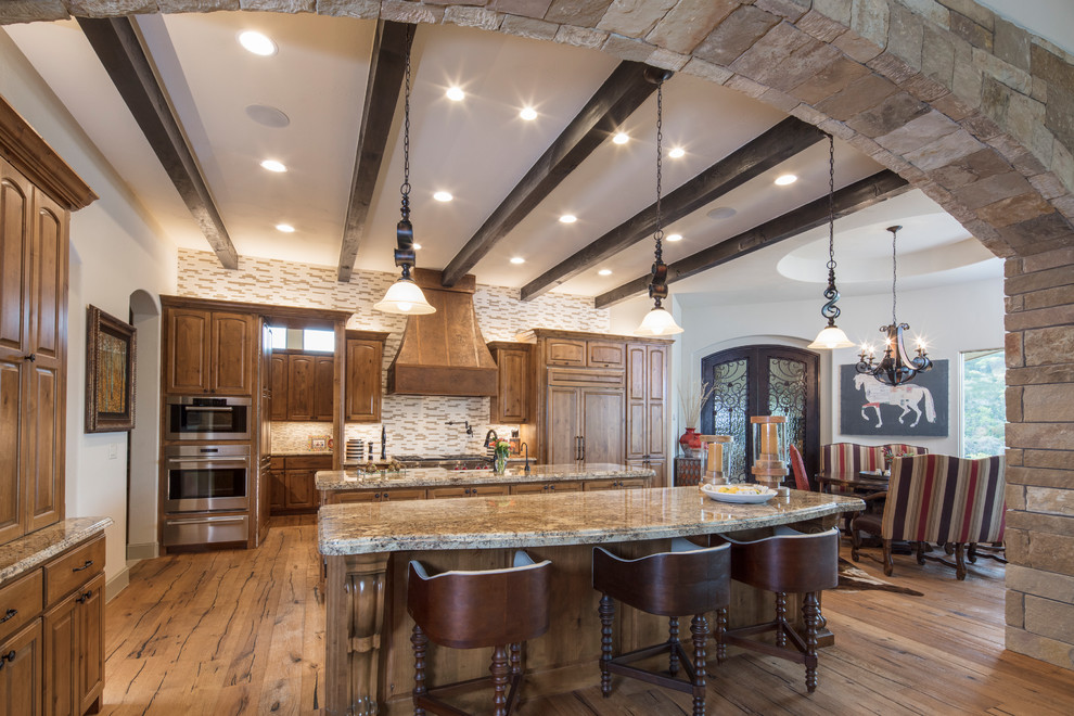 Large tuscan l-shaped light wood floor kitchen pantry photo in Austin with a double-bowl sink, raised-panel cabinets, light wood cabinets, granite countertops, multicolored backsplash, stone tile backsplash, stainless steel appliances and two islands