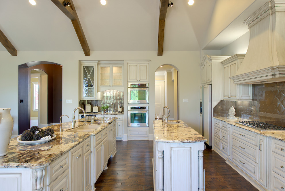 Inspiration for a mid-sized timeless galley medium tone wood floor eat-in kitchen remodel in Austin with a double-bowl sink, raised-panel cabinets, white cabinets, granite countertops, metallic backsplash, metal backsplash, paneled appliances and an island