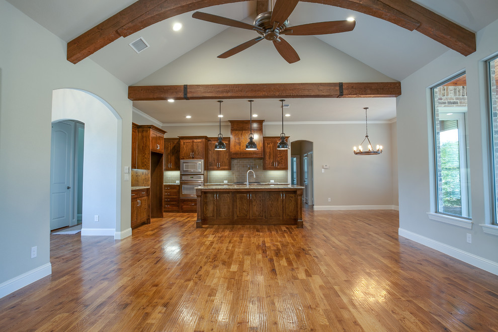 Inspiration for a large craftsman l-shaped medium tone wood floor open concept kitchen remodel in Dallas with a double-bowl sink, shaker cabinets, medium tone wood cabinets, granite countertops, beige backsplash, subway tile backsplash, stainless steel appliances and an island