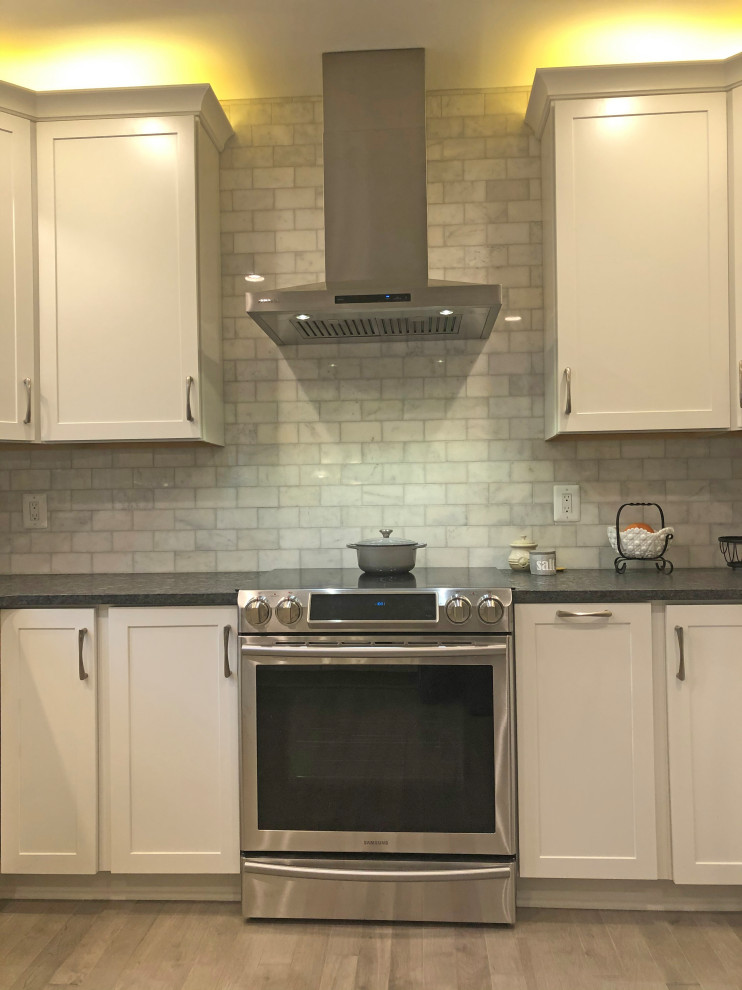 Klassisk inredning av ett litet grå grått kök, med en dubbel diskho, skåp i shakerstil, vita skåp, granitbänkskiva, grått stänkskydd, stänkskydd i marmor, rostfria vitvaror, ljust trägolv, en halv köksö och beiget golv