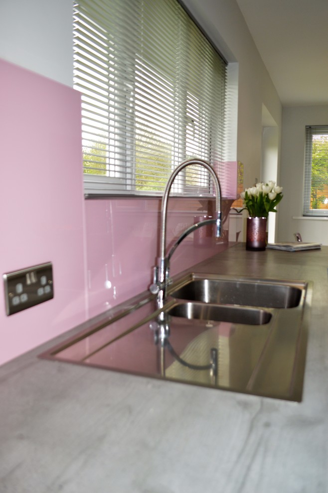 Стильный дизайн: п-образная кухня среднего размера в современном стиле с обеденным столом, накладной мойкой, плоскими фасадами, серыми фасадами, столешницей из ламината, розовым фартуком, фартуком из стекла, черной техникой и полуостровом - последний тренд