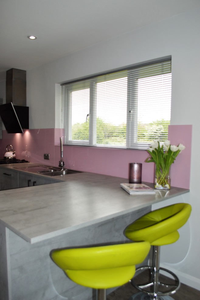 На фото: п-образная кухня среднего размера в современном стиле с обеденным столом, накладной мойкой, плоскими фасадами, серыми фасадами, столешницей из ламината, розовым фартуком, фартуком из стекла, черной техникой и полуостровом