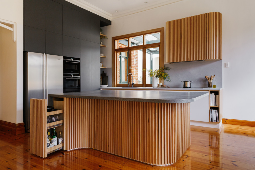 Inspiration for a medium sized midcentury l-shaped kitchen/diner in Adelaide with a submerged sink, flat-panel cabinets, black cabinets, composite countertops, grey splashback, stone slab splashback, integrated appliances, light hardwood flooring, an island, brown floors and grey worktops.