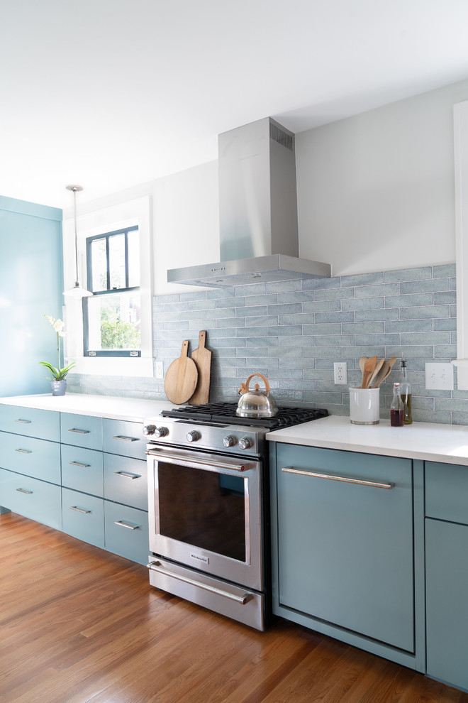 Modern inredning av ett mellanstort vit vitt kök, med en undermonterad diskho, släta luckor, blå skåp, bänkskiva i kvarts, blått stänkskydd, stänkskydd i keramik, rostfria vitvaror, mellanmörkt trägolv, en köksö och brunt golv