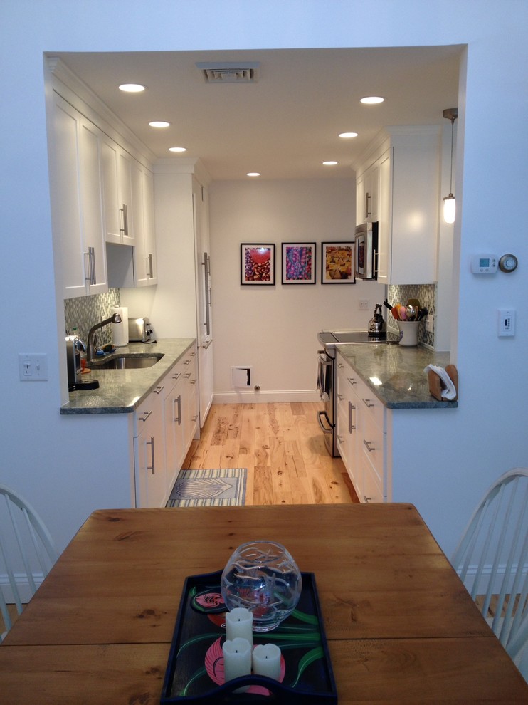 Bild på ett avskilt, litet funkis u-kök, med en undermonterad diskho, skåp i shakerstil, vita skåp, laminatbänkskiva, grönt stänkskydd, stänkskydd i mosaik, integrerade vitvaror, mellanmörkt trägolv och brunt golv