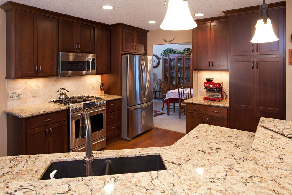 Inspiration for a mid-sized timeless l-shaped medium tone wood floor enclosed kitchen remodel in Minneapolis with an undermount sink, recessed-panel cabinets, medium tone wood cabinets, quartz countertops, beige backsplash, stone tile backsplash, stainless steel appliances and an island