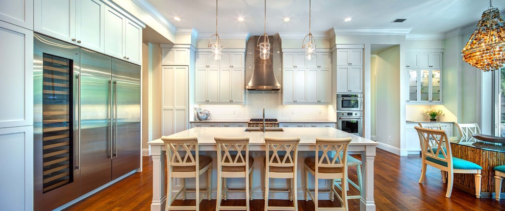 Beach style l-shaped medium tone wood floor and brown floor open concept kitchen photo in Tampa with a single-bowl sink, shaker cabinets, white cabinets, quartz countertops, white backsplash, porcelain backsplash, stainless steel appliances and an island