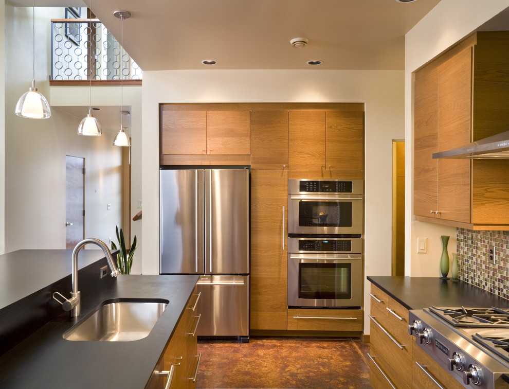 Foto på ett funkis kök, med stänkskydd i mosaik, rostfria vitvaror, flerfärgad stänkskydd, skåp i mellenmörkt trä, släta luckor och en undermonterad diskho