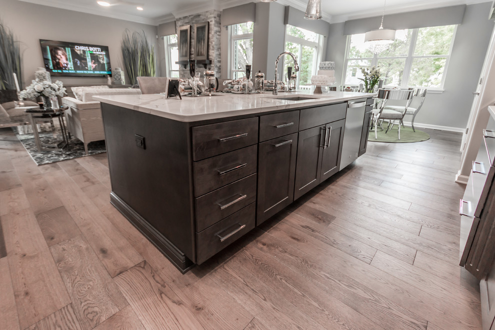 Inspiration for a medium sized traditional open plan kitchen in Milwaukee with a submerged sink, shaker cabinets, grey cabinets, engineered stone countertops, white splashback, marble splashback, stainless steel appliances, medium hardwood flooring, an island, brown floors and white worktops.