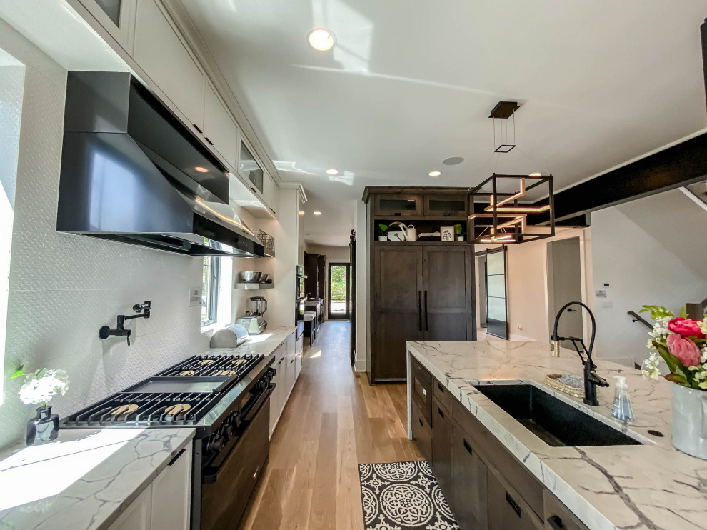 Photo of an expansive urban kitchen/diner in Chicago with a built-in sink, shaker cabinets, white cabinets, engineered stone countertops, grey splashback, black appliances, light hardwood flooring, an island, white worktops, a wood ceiling and mosaic tiled splashback.