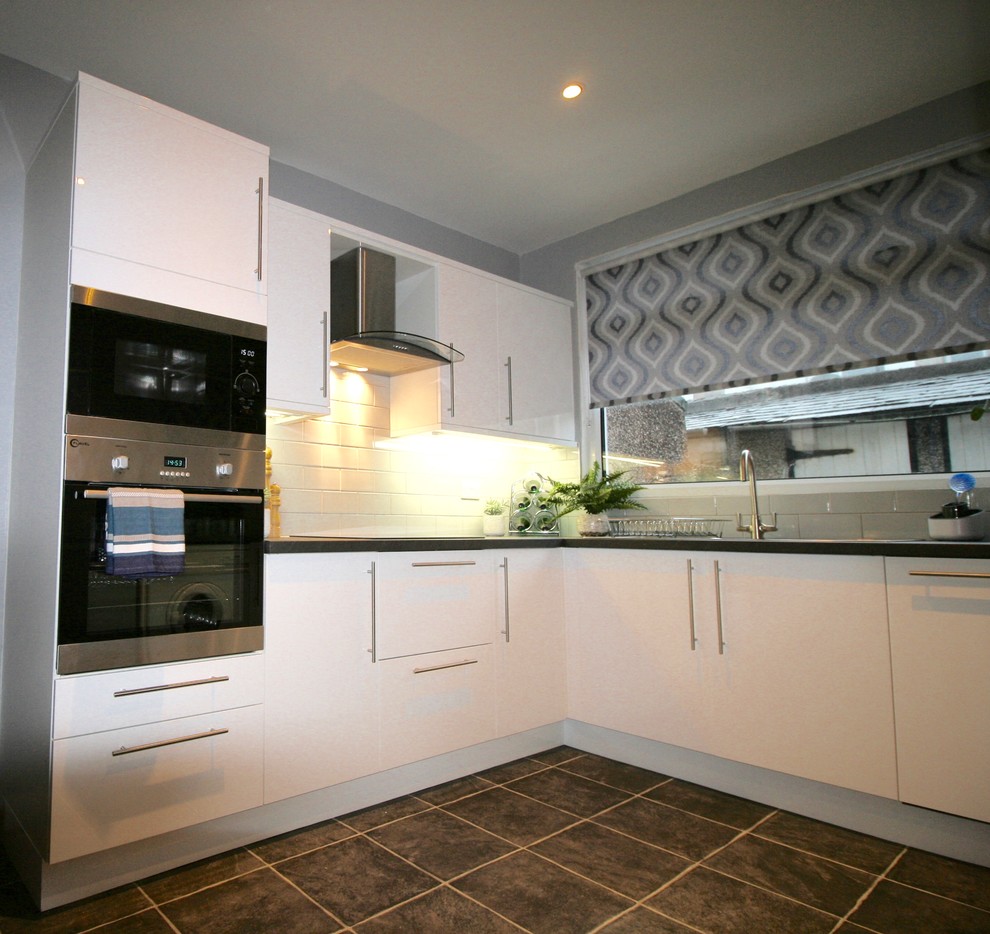This is an example of a medium sized contemporary u-shaped enclosed kitchen in Other with a built-in sink, flat-panel cabinets, white cabinets, laminate countertops, grey splashback, ceramic splashback, black appliances, vinyl flooring and no island.