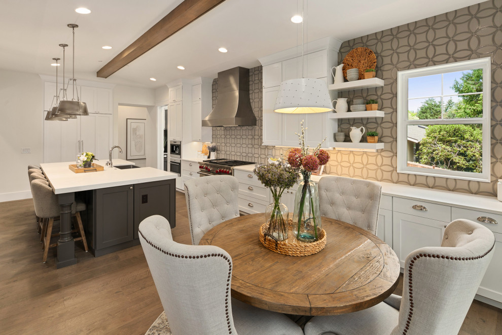 Inspiration for a large classic single-wall kitchen/diner in Seattle with a belfast sink, shaker cabinets, white cabinets, quartz worktops, grey splashback, porcelain splashback, stainless steel appliances, medium hardwood flooring, an island, brown floors, white worktops and exposed beams.