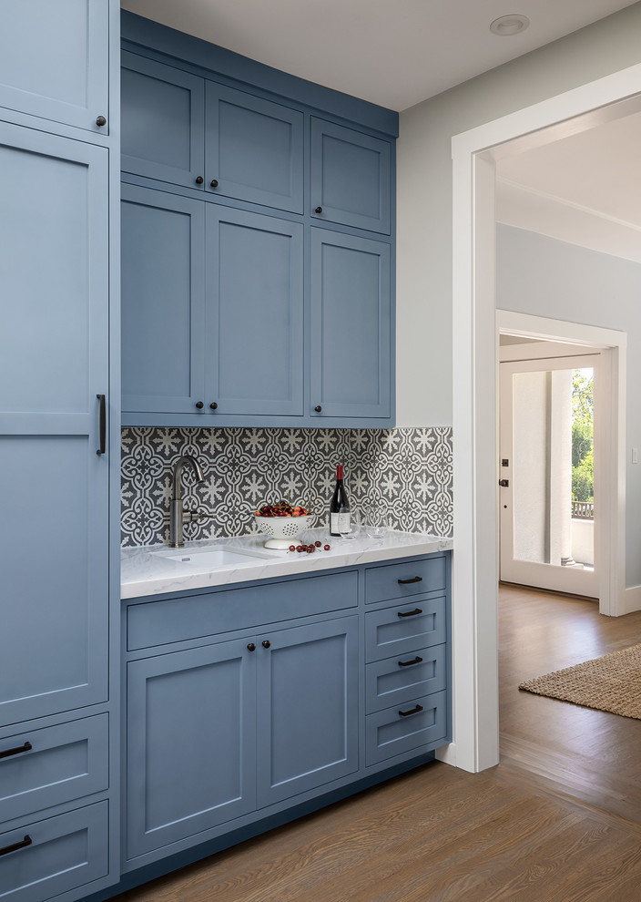 На фото: кухня в стиле неоклассика (современная классика) с фасадами в стиле шейкер, синими фасадами, столешницей из кварцевого агломерата, фартуком из цементной плитки и белой столешницей
